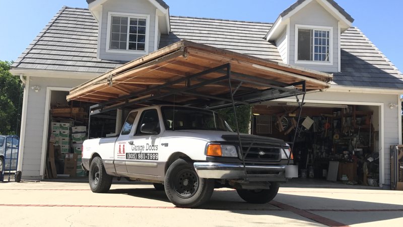 AA Garage Doors' original white Ford Ranger work truck with an old garage door on the overhead rack, AA logo and (805) 981-7999 on the door