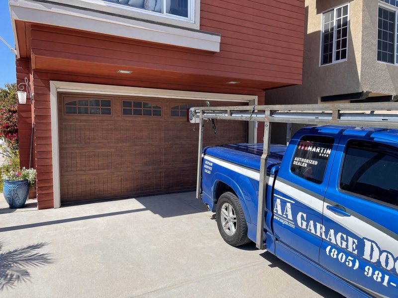 AA Garage Doors service truck parked beside a newly installed wood-grain garage door with arched windows