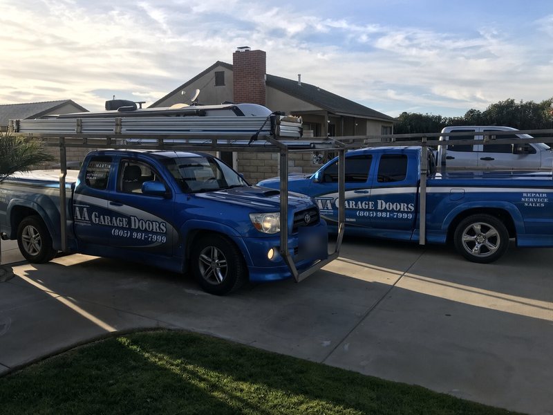 Two blue AA Garage Doors Toyota Tacoma service trucks with ladder racks, lettered with the company name and (805) 981-7999
