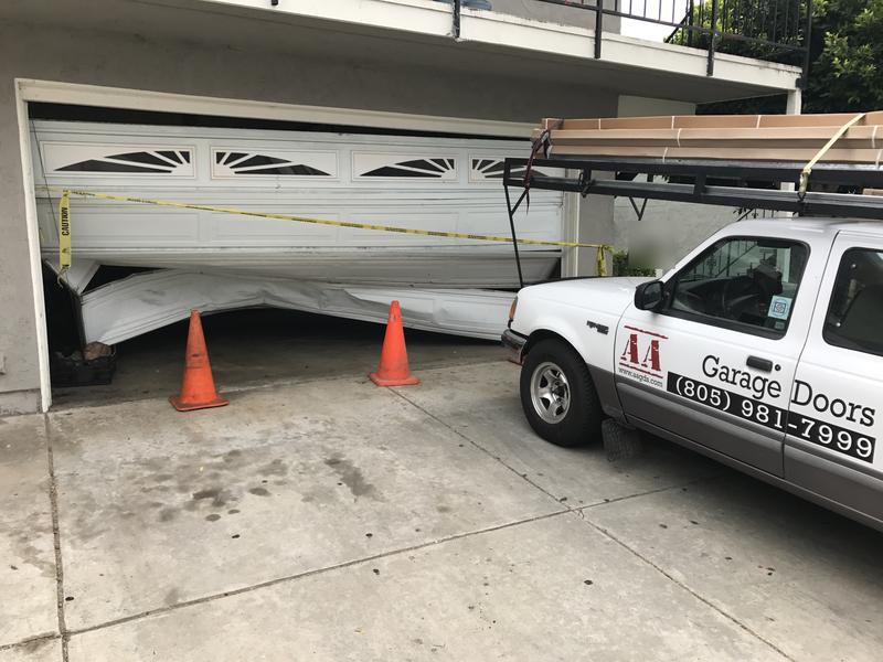 White garage door crushed after being hit by a car, taped off with cones, next to AA Garage Doors' first work truck