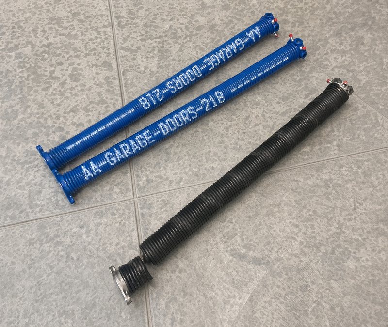 Broken black torsion spring next to two new blue AA Garage Doors springs