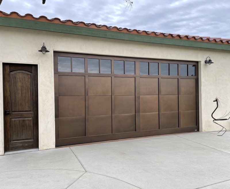 Bronze carriage-style garage door with window tops next to a matching wood side entry door