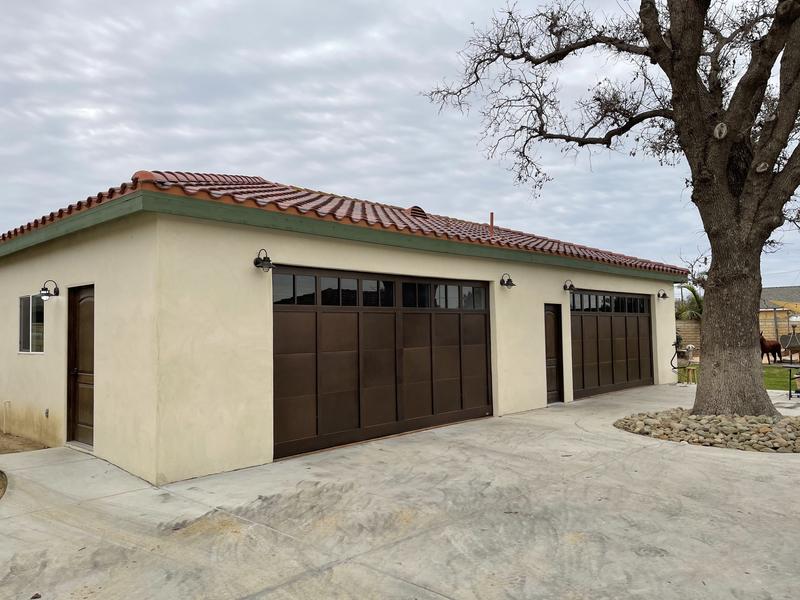 Wide view of a stucco garage with two bronze carriage-style garage doors and a red tile roof