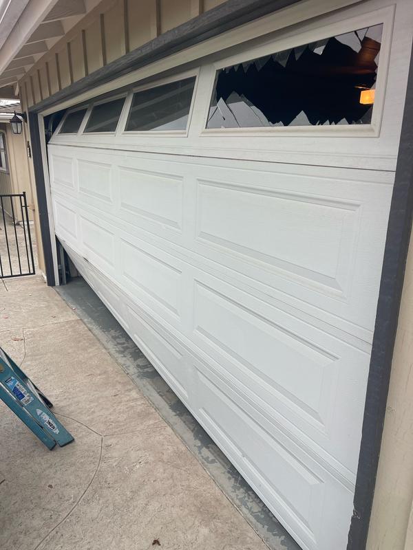 White garage door with a smashed window, pushed off its track