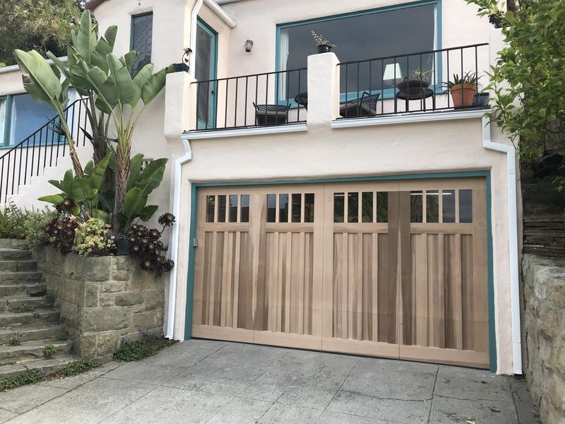 Natural wood carriage-style garage door with a row of windows across the top