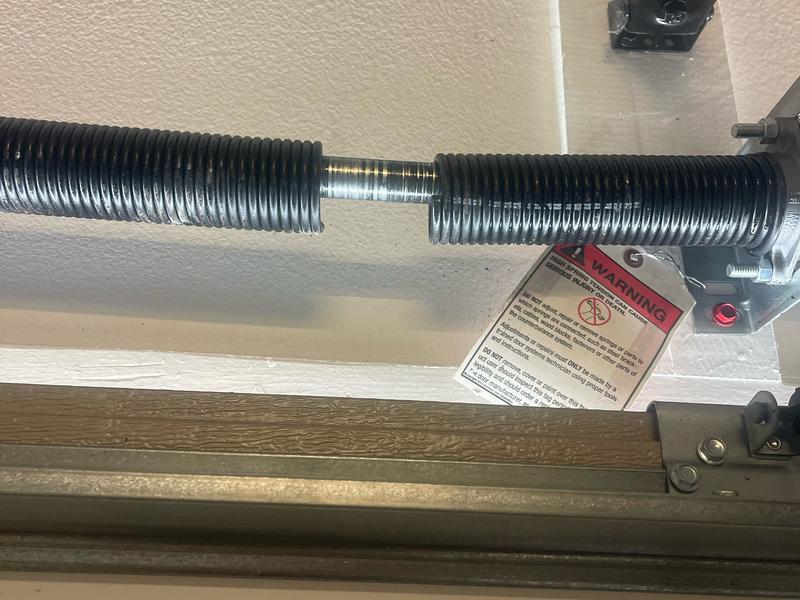 Snapped torsion spring on the shaft above a garage door, with a visible gap