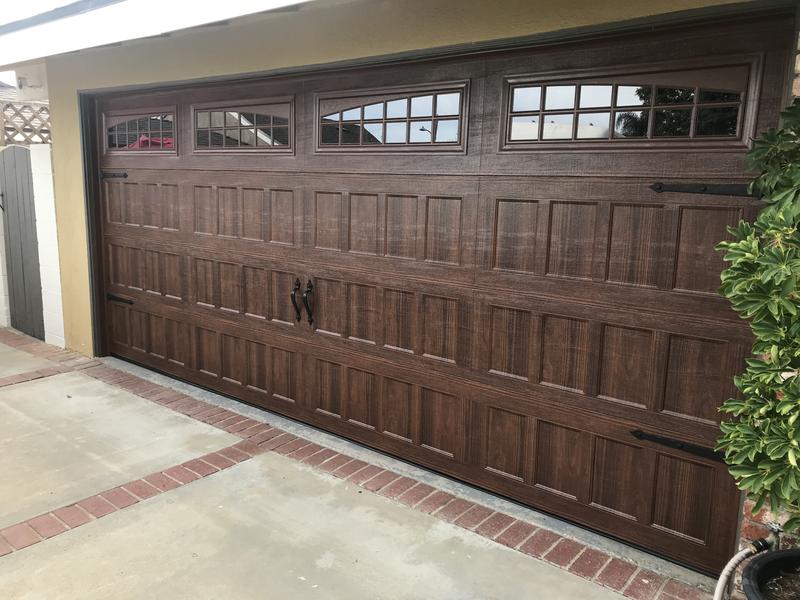 Walnut wood-grain carriage-style garage door with arched windows and black hardware