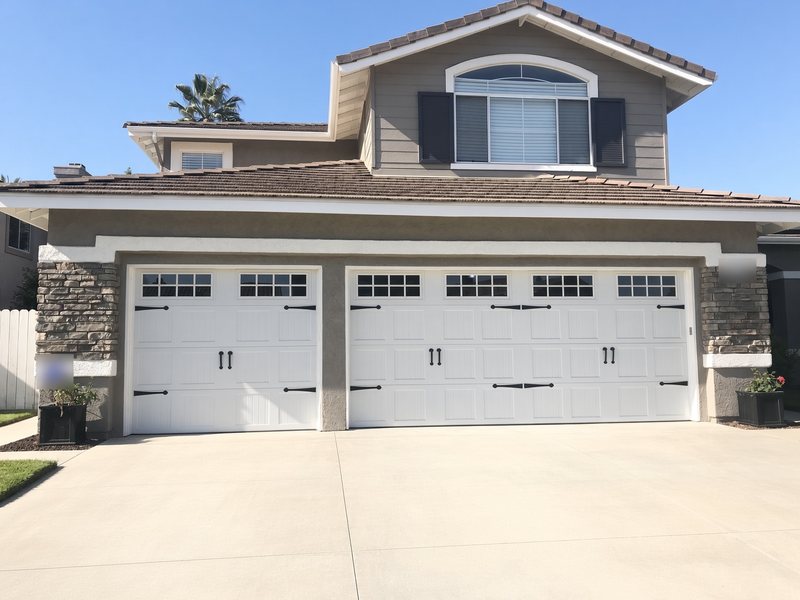 Three-car garage with white carriage-style doors, window tops and black decorative hardware between stone columns
